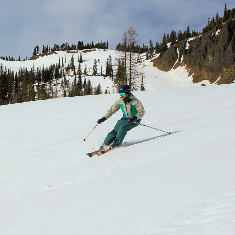 a skier carves the cords on a sunny spring day in front of basalt cliffs
