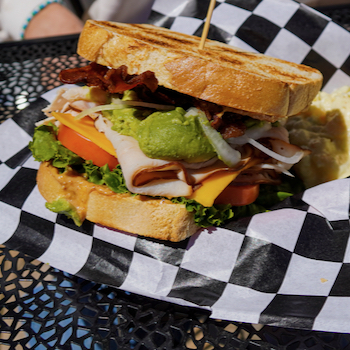 Image of a club sandwich including lettuce, turkey, tomato, bacon, onion, and cheese.