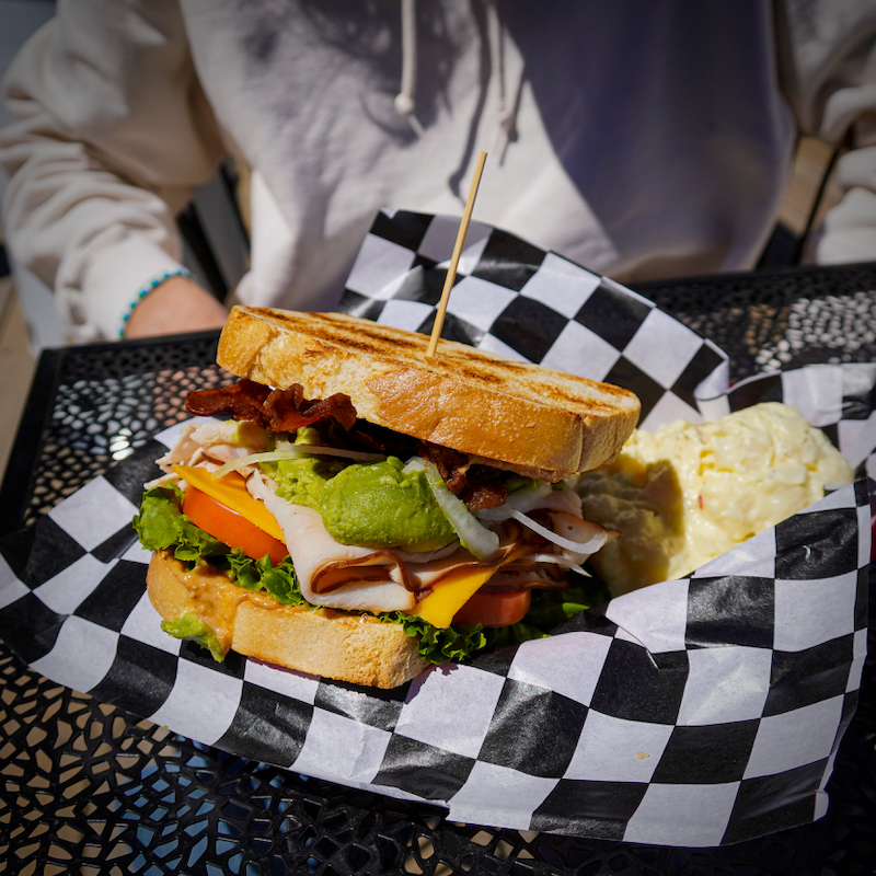 A club sandwich with turkey, avocado, lettuce, tomato, and cheese sitting in a checker-colored serving paper.