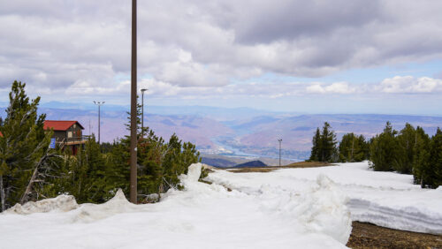 A view of a snow mountaintop looking down into an open valley with a river below. 