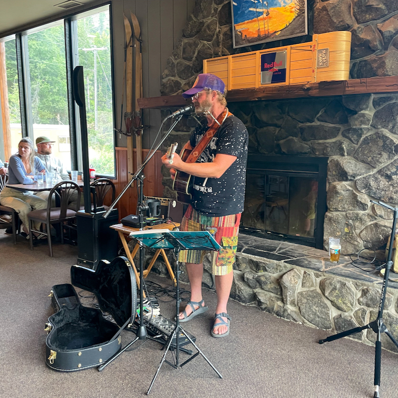 Local musician Rib plays his guitar and sings into the microphone in front of the Hampton Lodge fireplace.