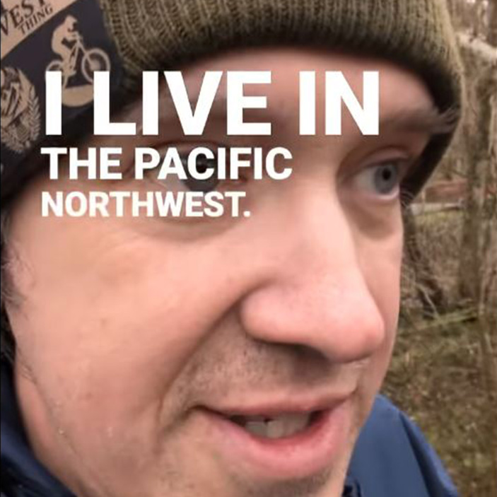 A close-up image of a man wearing a beanie and jacket, set in a wooded outdoor area. Overlaid in bold white text are the words: “I LIVE IN THE PACIFIC NORTHWEST.” The photo has a humorous tone, commonly associated with memes that highlight the quirks of Pacific Northwest life, such as the rainy weather, outdoor culture, or regional stereotypes.