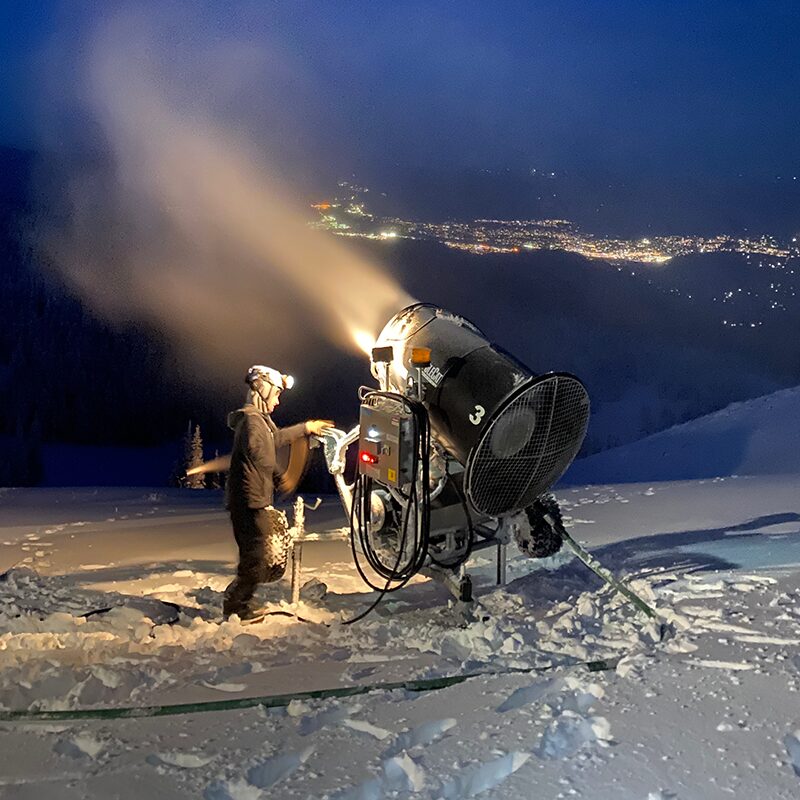 Snowgun making snow at night with snowmaker standing near by