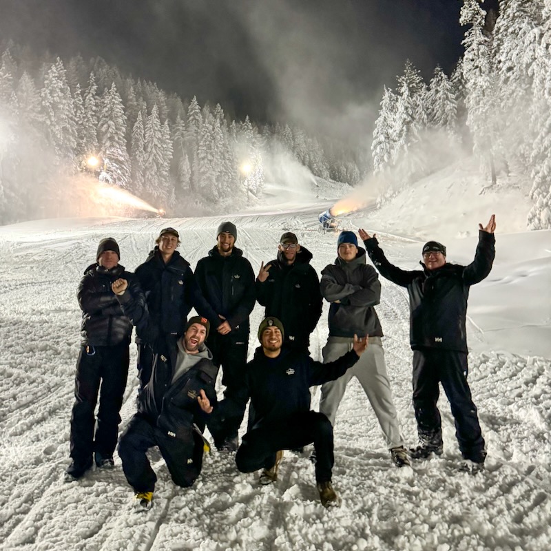 A photo of the Mission Ridge snowmaking crew at night in front of snow guns and night lights on the mountain.