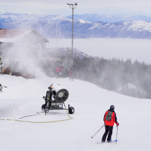 photo from the summit of mission ridge, including a patroller skiing toward a snow gun and the summit lift shack.