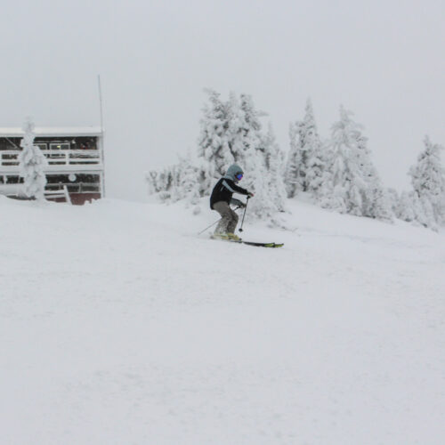 A skier carves past a snowy shack