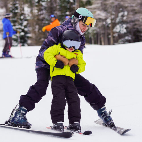 a woman steadies a child as they ski together