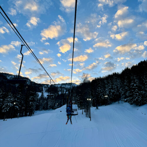 Skiers ride Chair 1 at Mission Ridge in late afternoon with patchy clouds overhead.