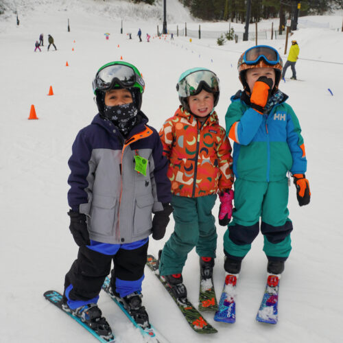 Three children on skis standing at the bottom of the beginners slope.