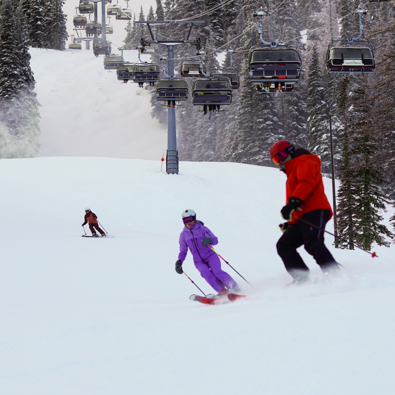 A few skiers carve up an overcast slope below a lift line