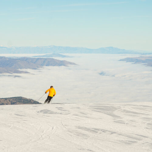 Skier descends the Sunspot trail at Mission Ridge above the clouds on a sunny day.