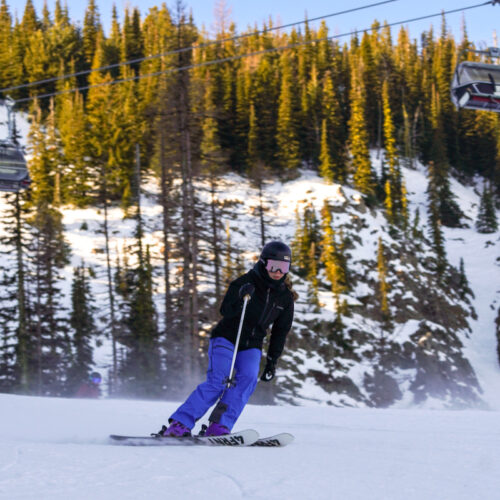A skier descends the Tumwater trail at Mission Ridge with sunny cliffs in the background.