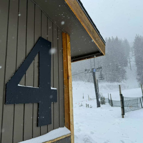 Snow falls beside a building marked with a large number “4” at Mission Ridge, with Chair 4 and snow-covered trees visible in the background during active winter conditions.