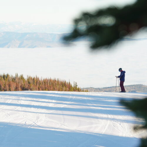 Skier standing on side of run above clouds.