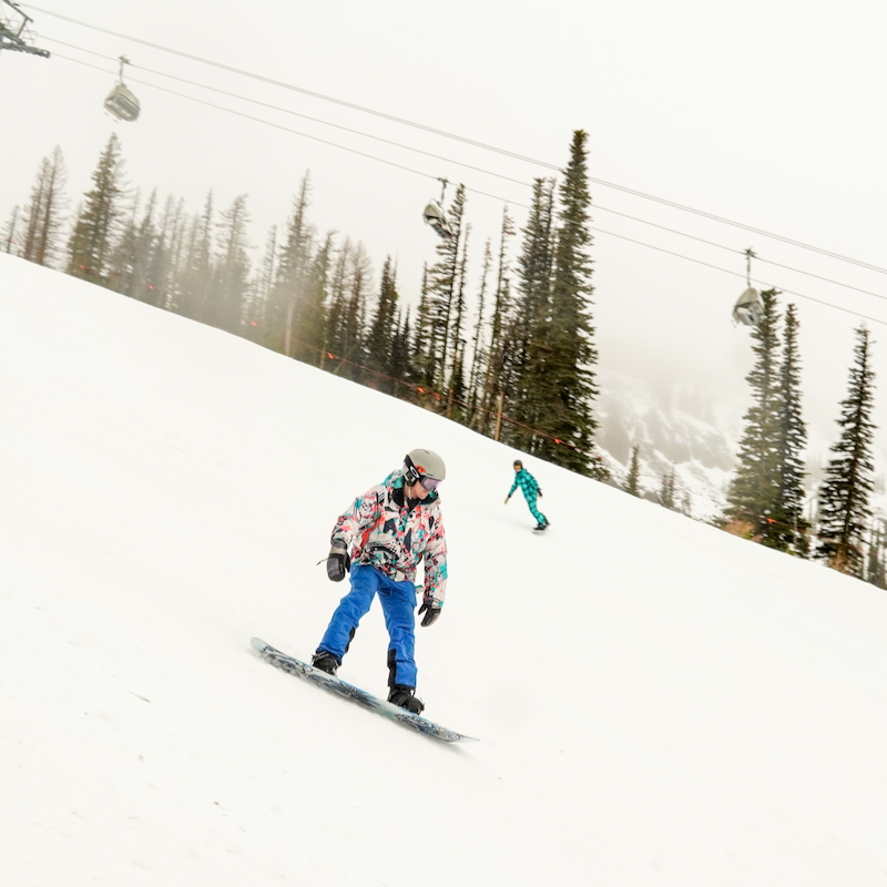 snowboarder in bright clothes slides below a chairlift