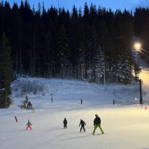 A family of skiers descends the Pika Peak learning area at Mission Ridge under the night lights