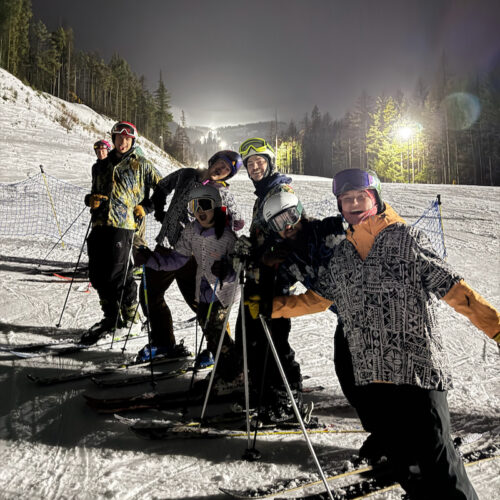 A group of skiers smiling at Mission Ridge, wearing Hawaiian shirts over their ski gear at night.