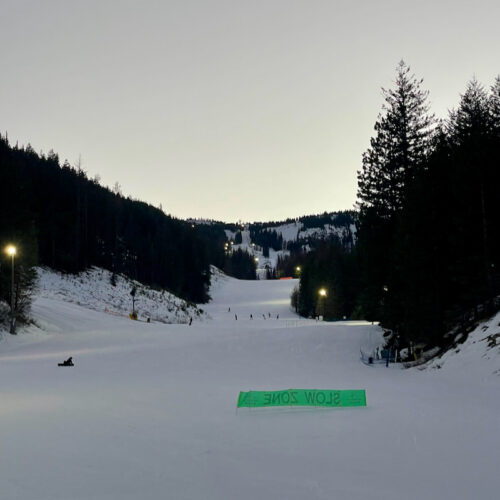 A view up the mountain at night at Mission Ridge, showing the Mimi run with a few skiers dotting the slopes.