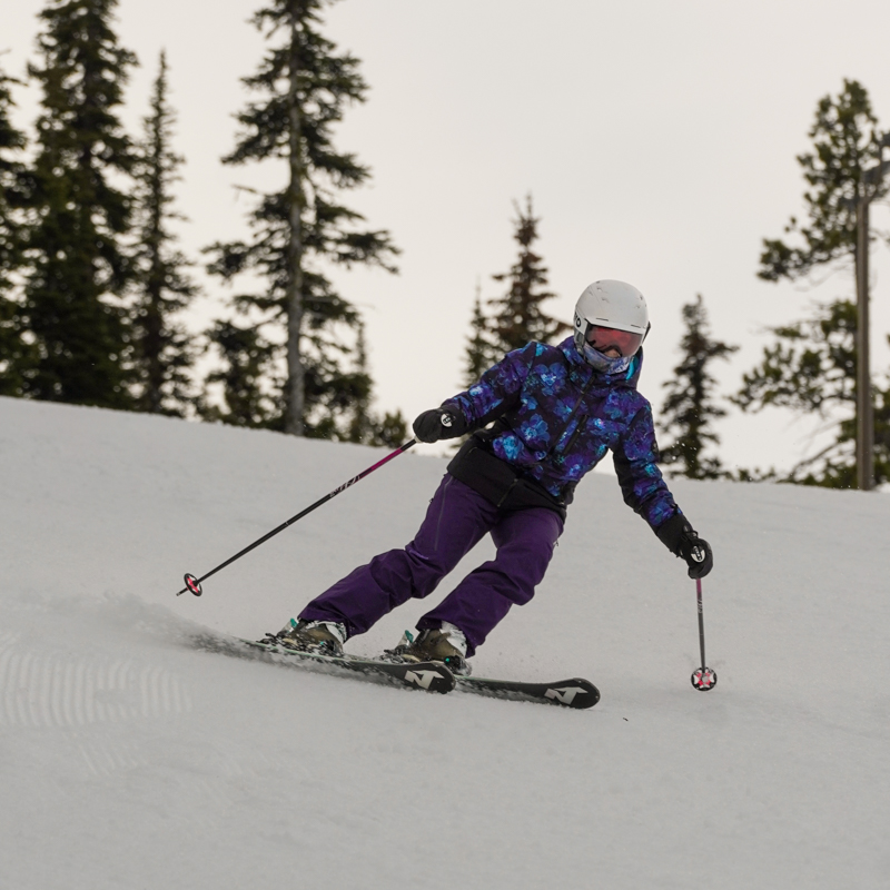 a skier in blue and purple carves an overcast slope