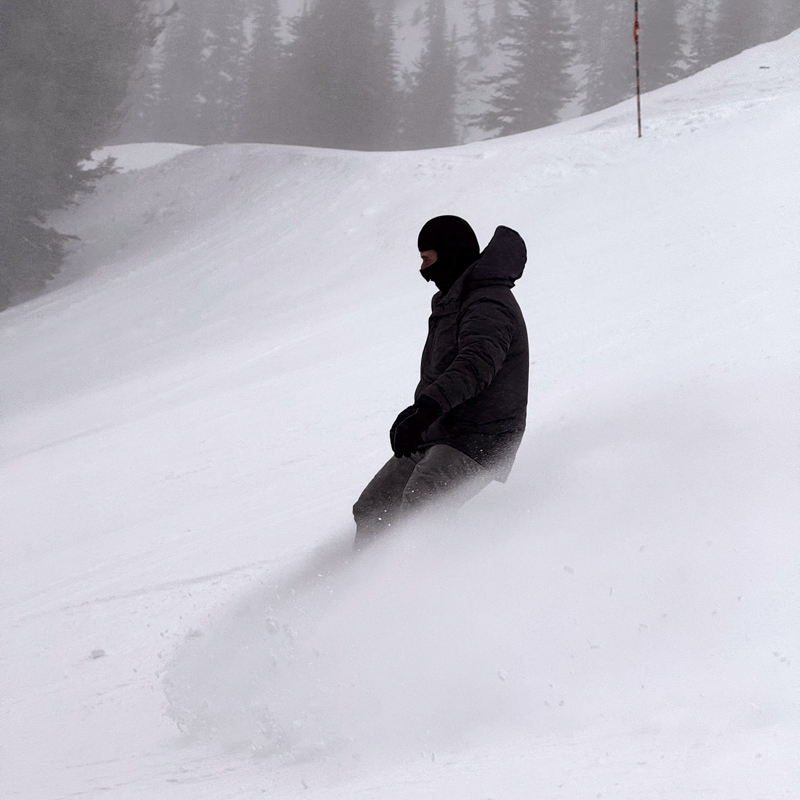 A snowboard kicks up a big spray on an overcast slope