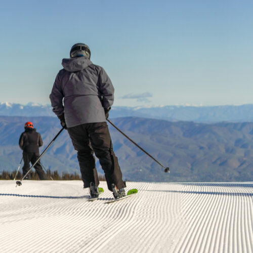 A skier in a grey jacket begins to descend thhe Sunspot trail at Mission Ridge on a sunny day.
