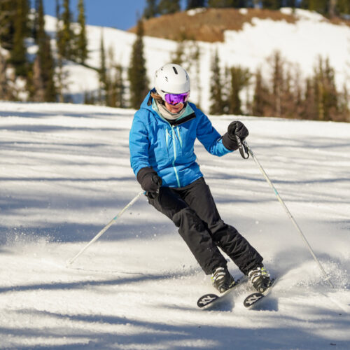 A skier in a blue jacket descends the Tumwater trail at Mission Ridge on a sunny day.
