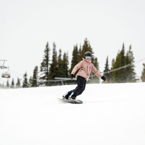 A snowboarder in a pink jacket descends the Tumwater trail at Mission Ridge on a cloudy day.
