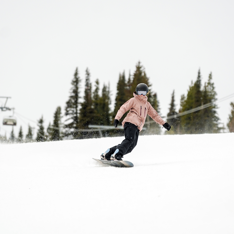 A snowboarder in a pink jacket descends the Tumwater trail at Mission Ridge on a cloudy day.