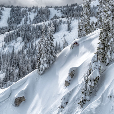 Skier dropping into a steep powder run through snow-covered trees at Mission Ridge Ski & Board Resort.