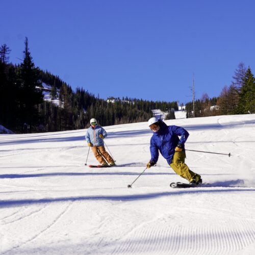 two skiers slide under coal t blue sky
