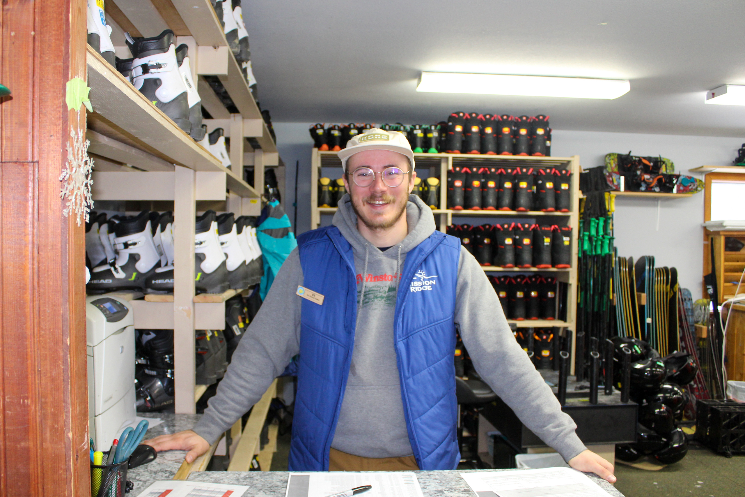 An employee of Mission Ridge stands smiling in front of the ski school rental gear.