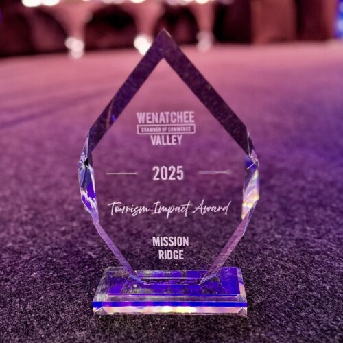 Crystal award with “Wenatchee Valley Chamber of Commerce 2025 Tourism Impact Award” engraved, presented to Mission Ridge, displayed on a carpeted surface with a softly lit, blurred background.