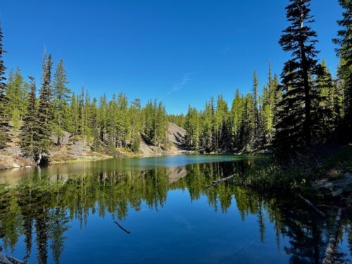 Lake Clara reflecting evergreen trees and a clear blue sky on a sunny spring morning.