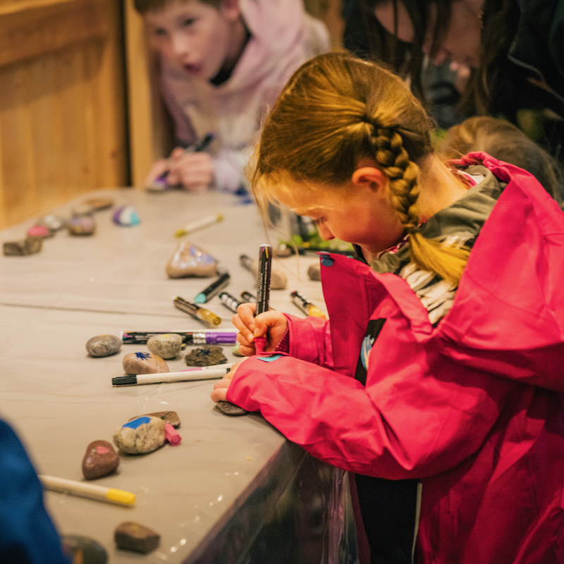 A child painting a rock at a craft table during Tamarack Festival
